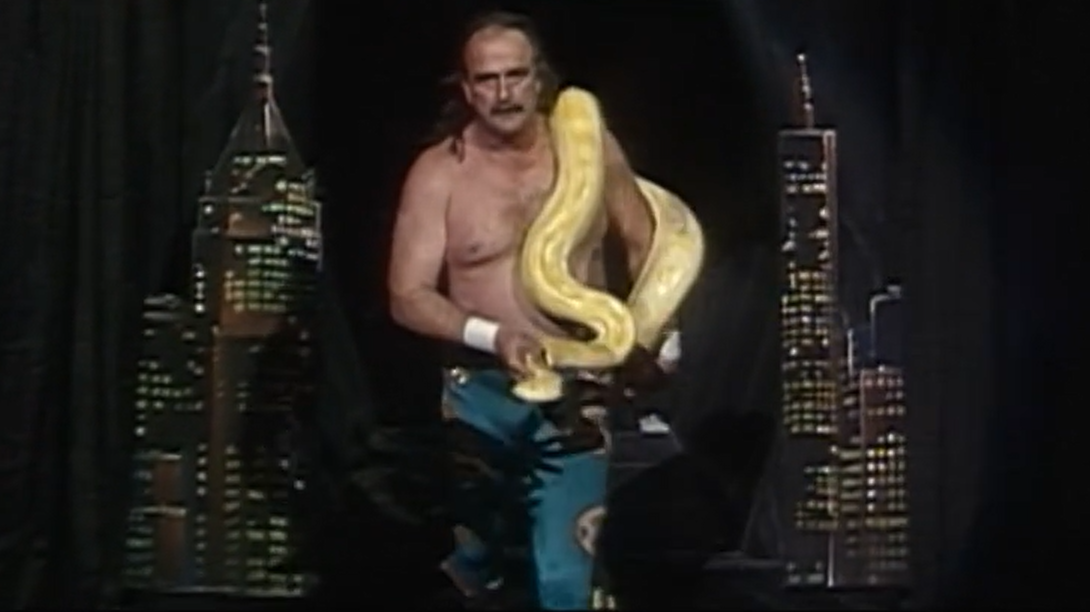 Jake Roberts enters through the building-adorned set, with yellow python.