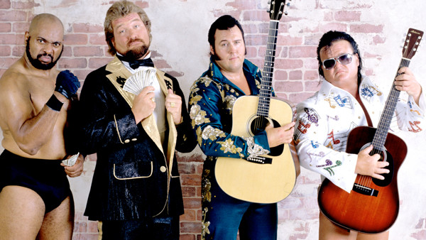 Bad News Brown stands posing next to Ted DiBiase and Rhythm & Blues.